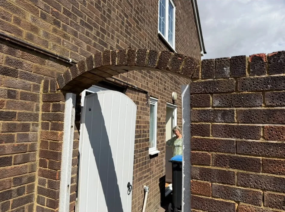 Brick arch over an open white side gate beside a brick house
