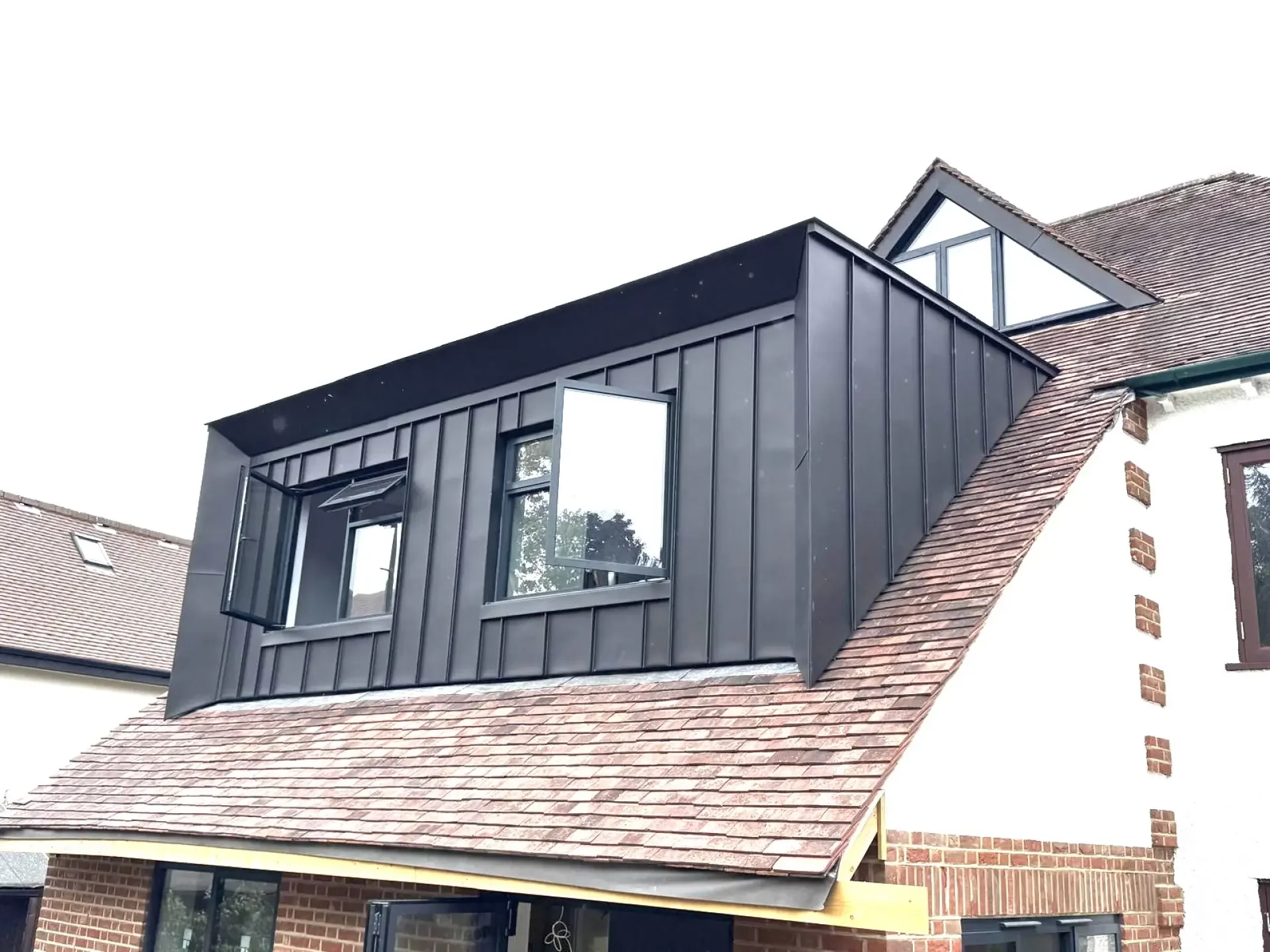 Black standing seam zinc dormer on a tiled roof in Wandsworth