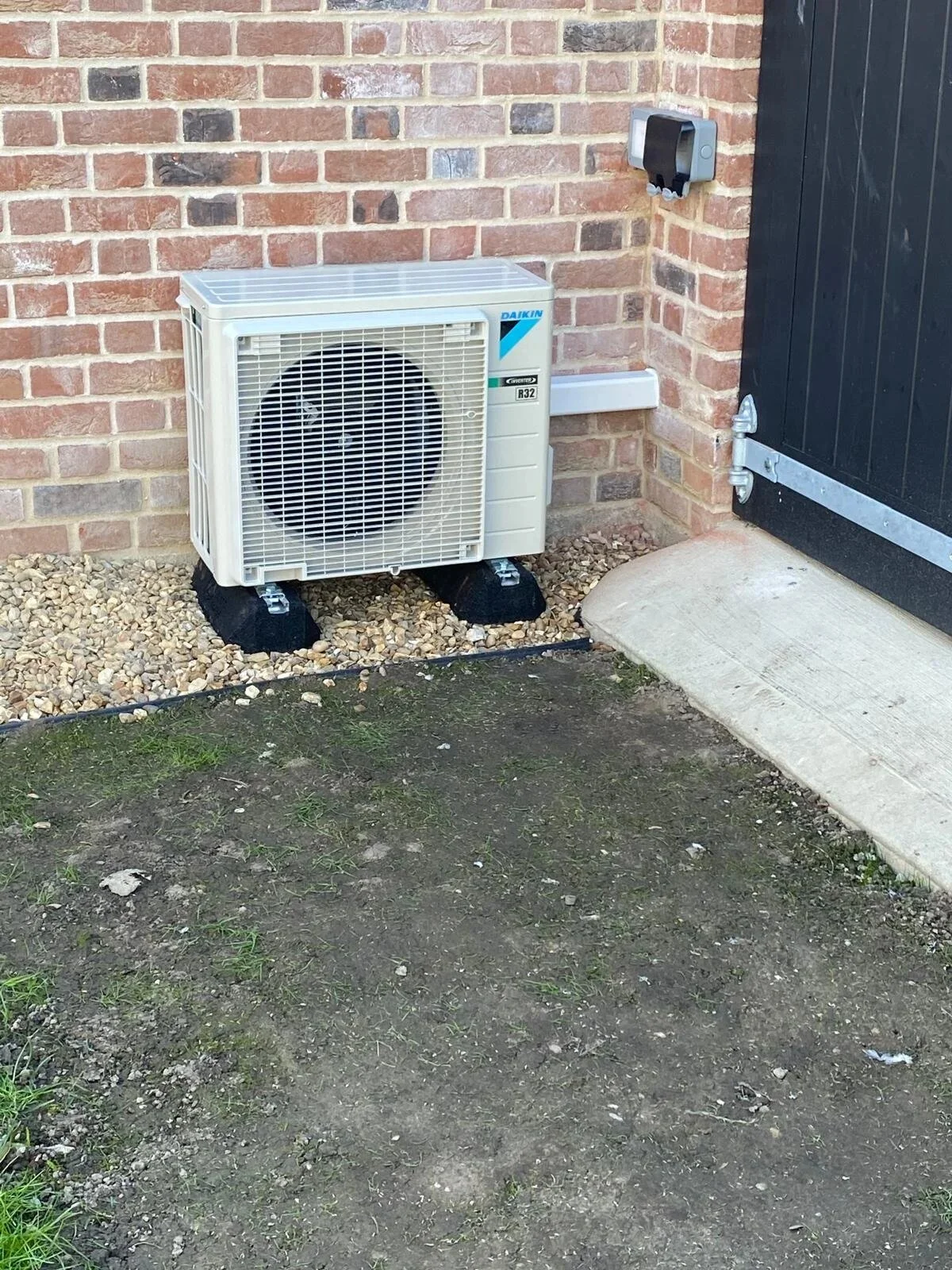 Air conditioning outdoor unit on stands beside a black barn door