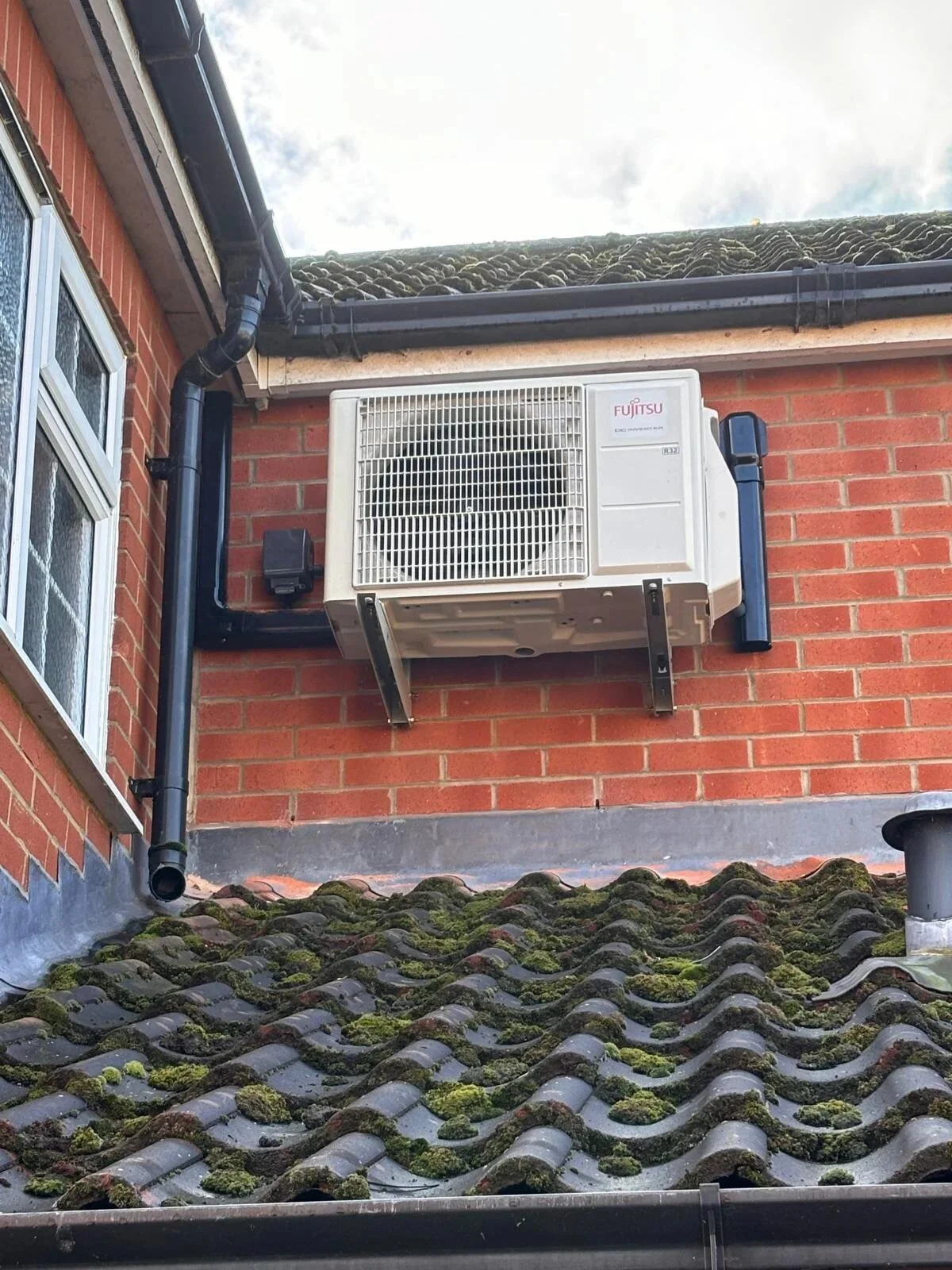 Air conditioning outdoor unit on a wall bracket above a roof