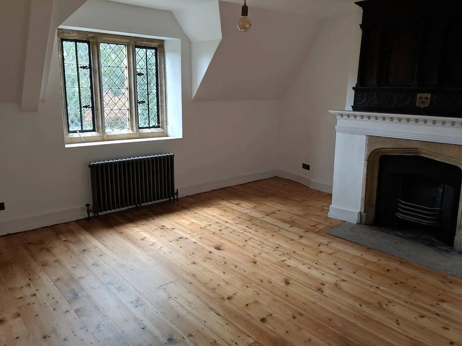 Cast iron radiator under a leaded window in a room with bare floorboards