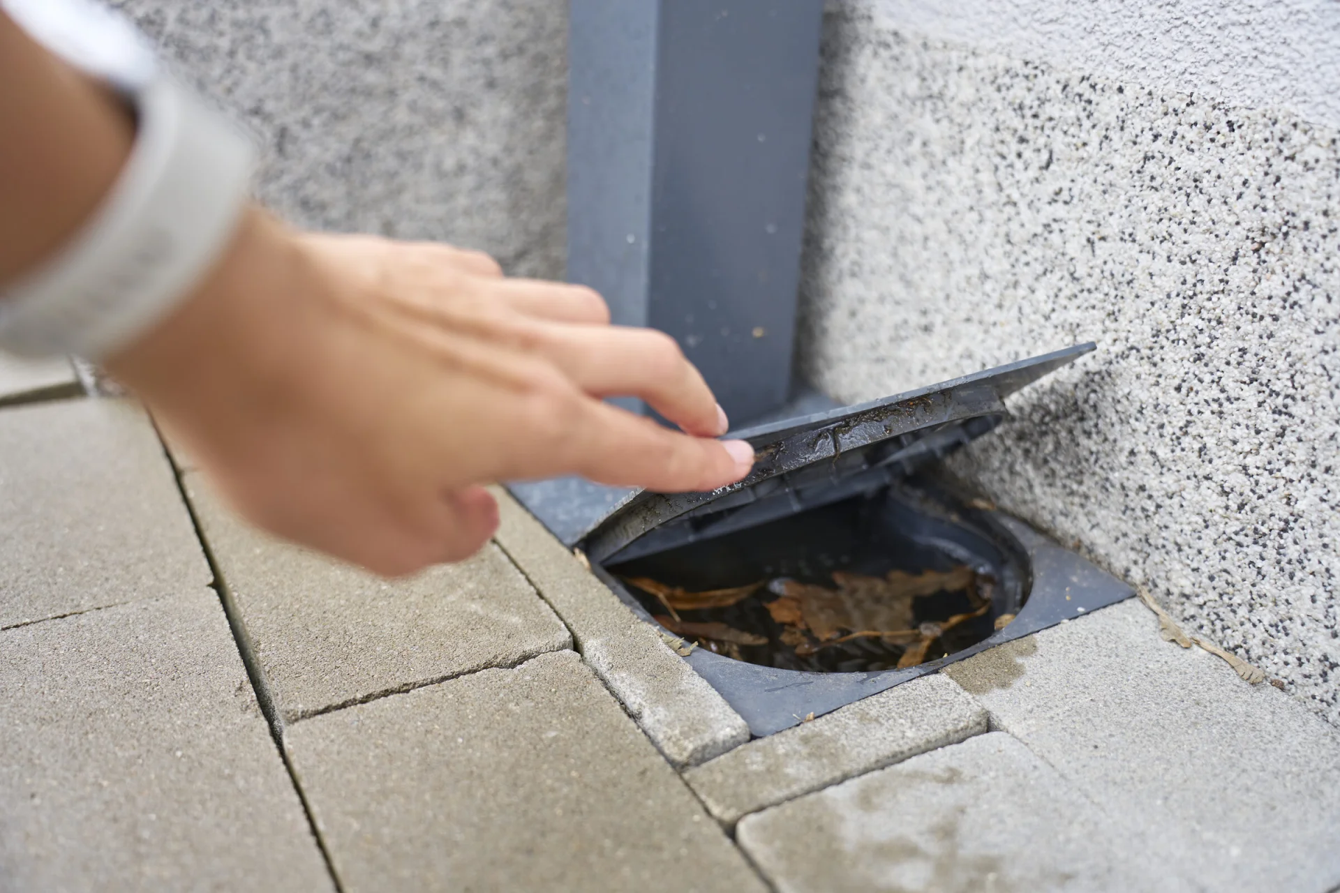 Lifting an outdoor drain cover full of leaves and debris