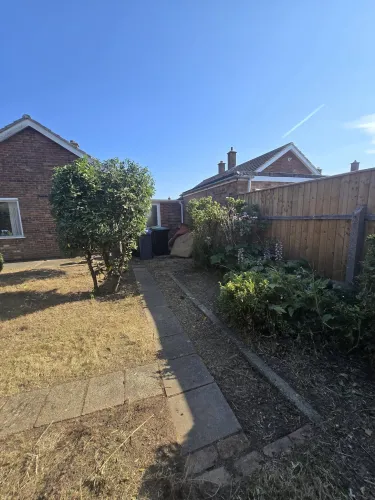 Tidied back garden with trimmed shrub, weeded border and cleared paved path beside a bungalow