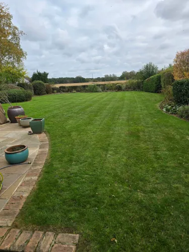 Large striped rear lawn stretching to a field boundary with a patio and planters